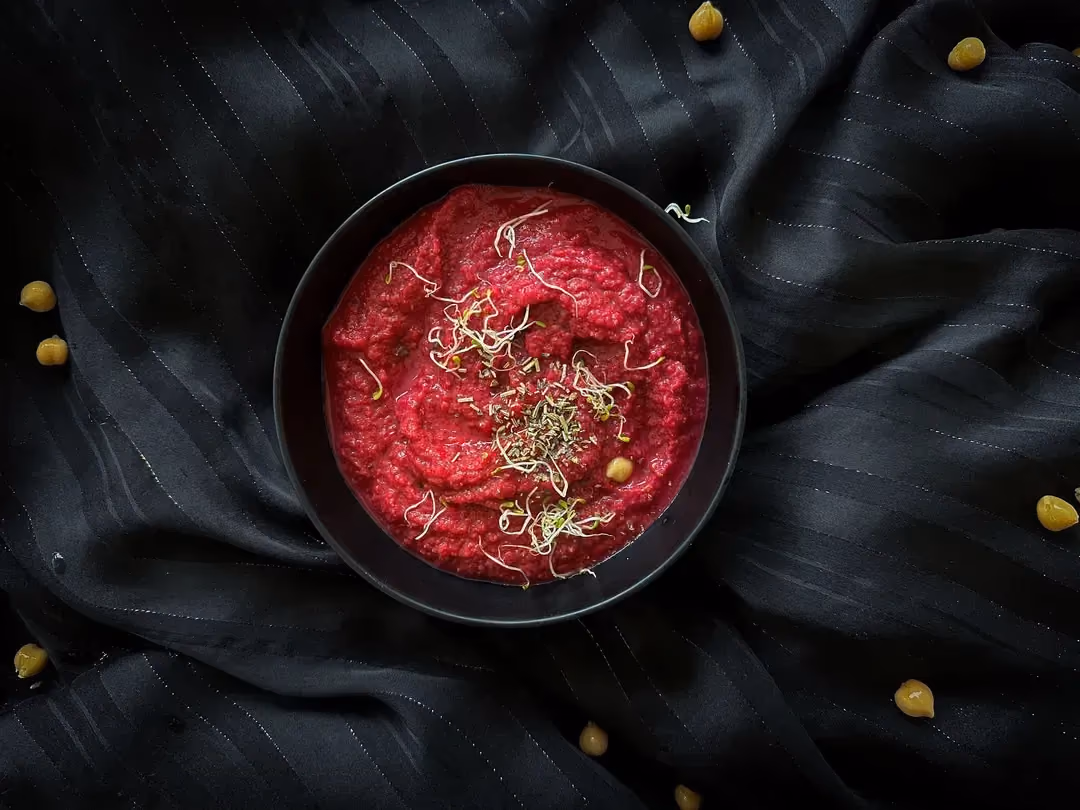 In a shallow white earthenware dish is a chickpea and beet purée. Julienned vegetables are arranged on one side.