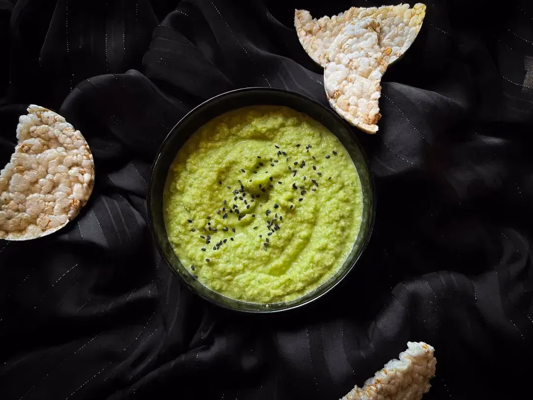 Zucchini hummus sprinkled with sesame seeds is served in a small blue bowl. The green sauce looks beautiful.
