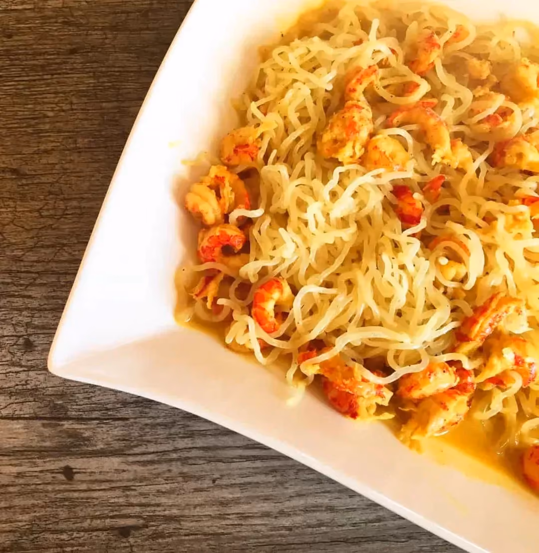 This recipe for konjac with shrimp, lemon, and coconut milk is presented in a large white earthenware dish.