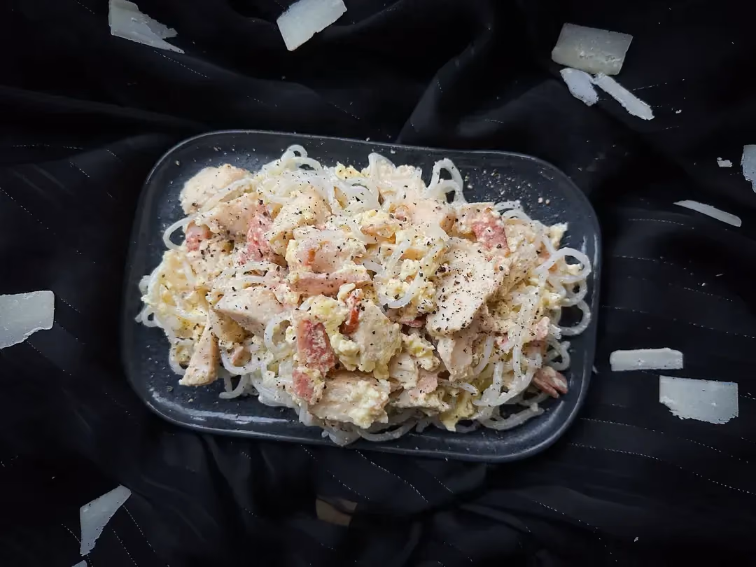 In a large bowl is konjac carbonara, a very creamy recipe. A fork has just dipped into the sauce.