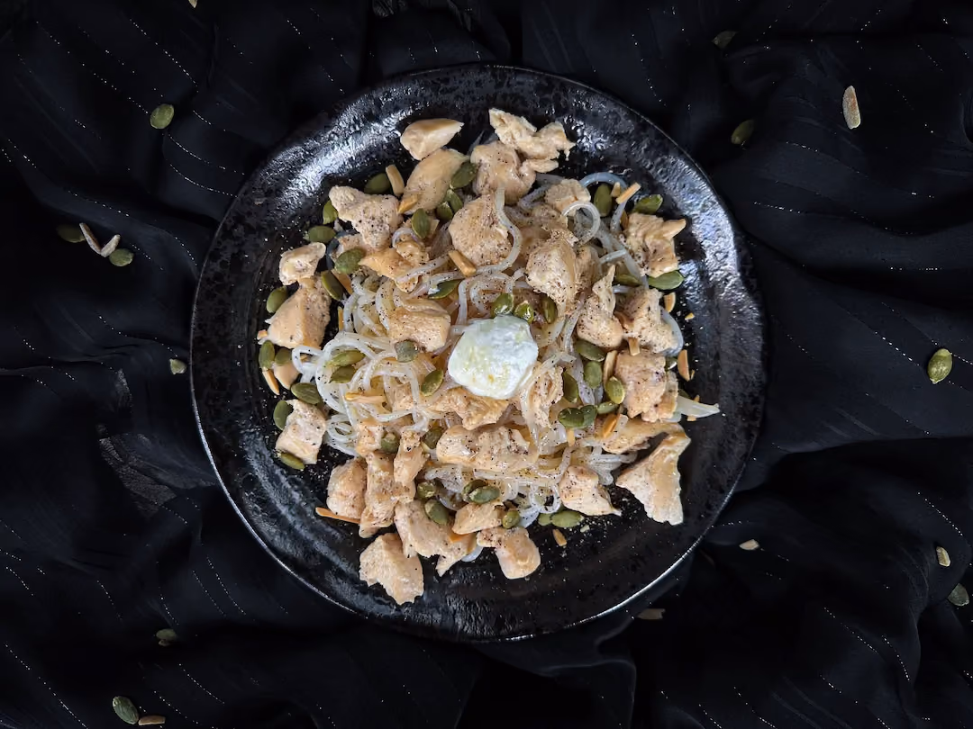 The recipe for konjac with chicken, goat cheese, honey, and pumpkin seeds is presented in a small blue earthenware bowl.