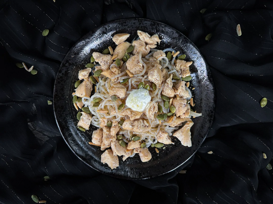 The recipe for konjac with chicken, goat cheese, honey, and pumpkin seeds is presented in a small blue earthenware bowl.