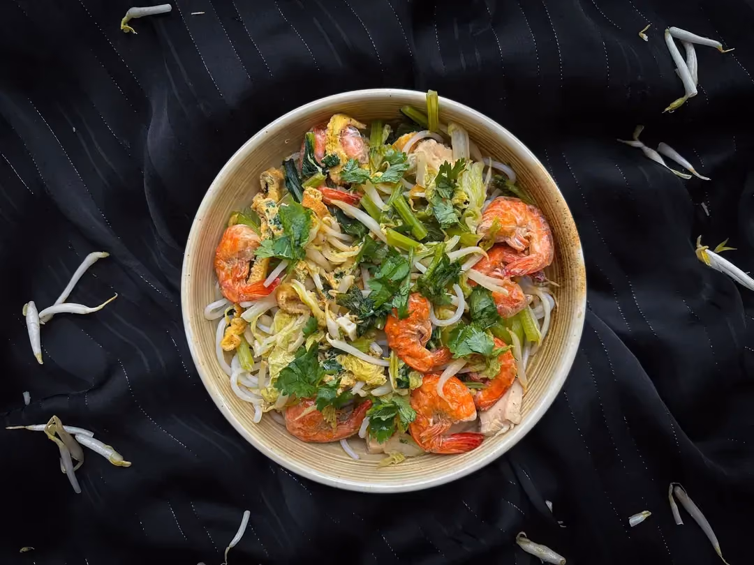 Le char kway teow est présenté dans un plat en grès. Deux baguettes sont présentent pour manger la préparation.