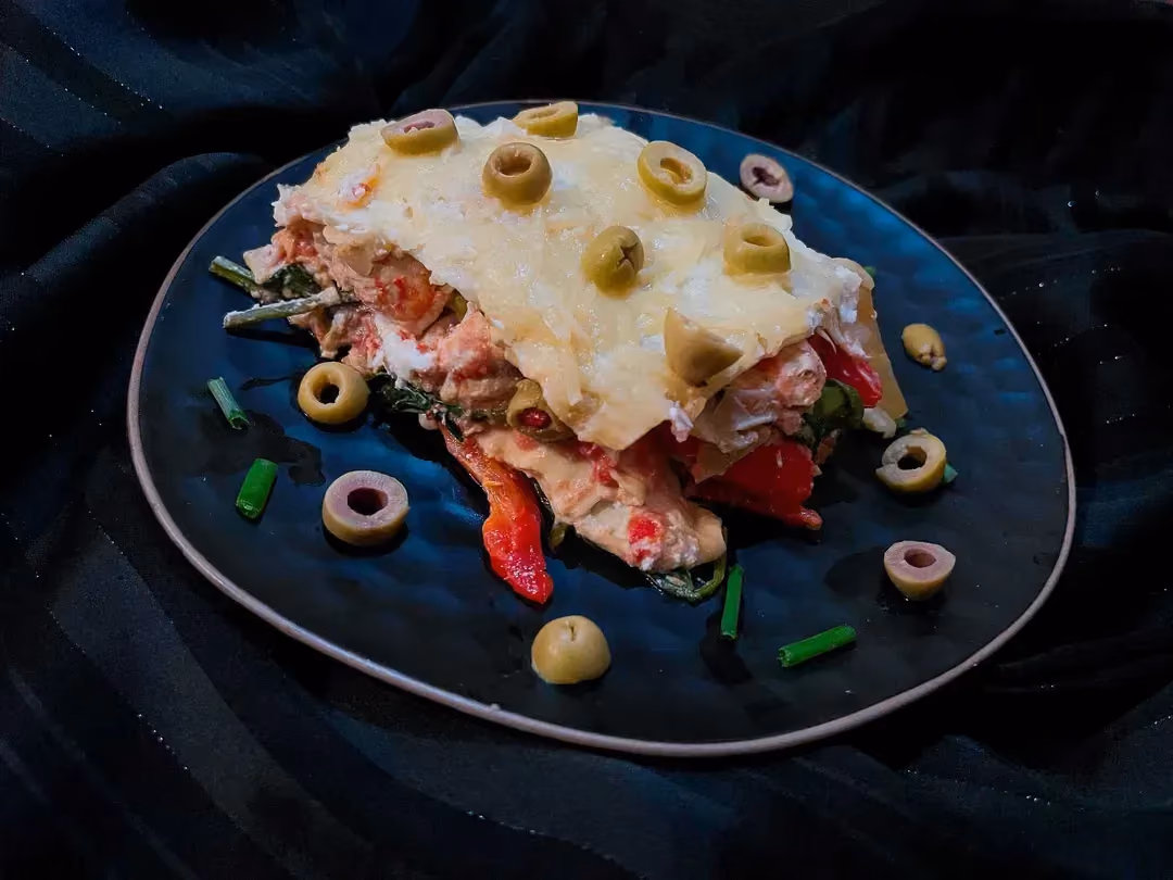Greek-style lasagna is arranged on a beautiful blue dish. A few sliced green olives complete the presentation