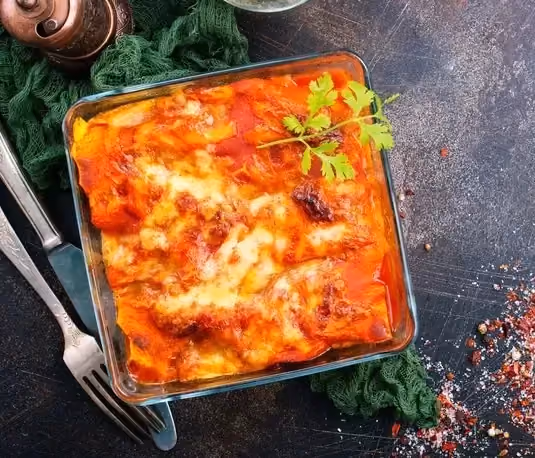 Posé sur un plan de travail de couleur anthracite les lasagnes à la patate douce sont dans un plat à gratin transparent de forme carré.