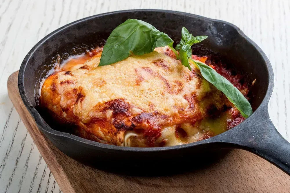 In a skillet, you'll find the lasagna. A few small basil leaves are placed on top.