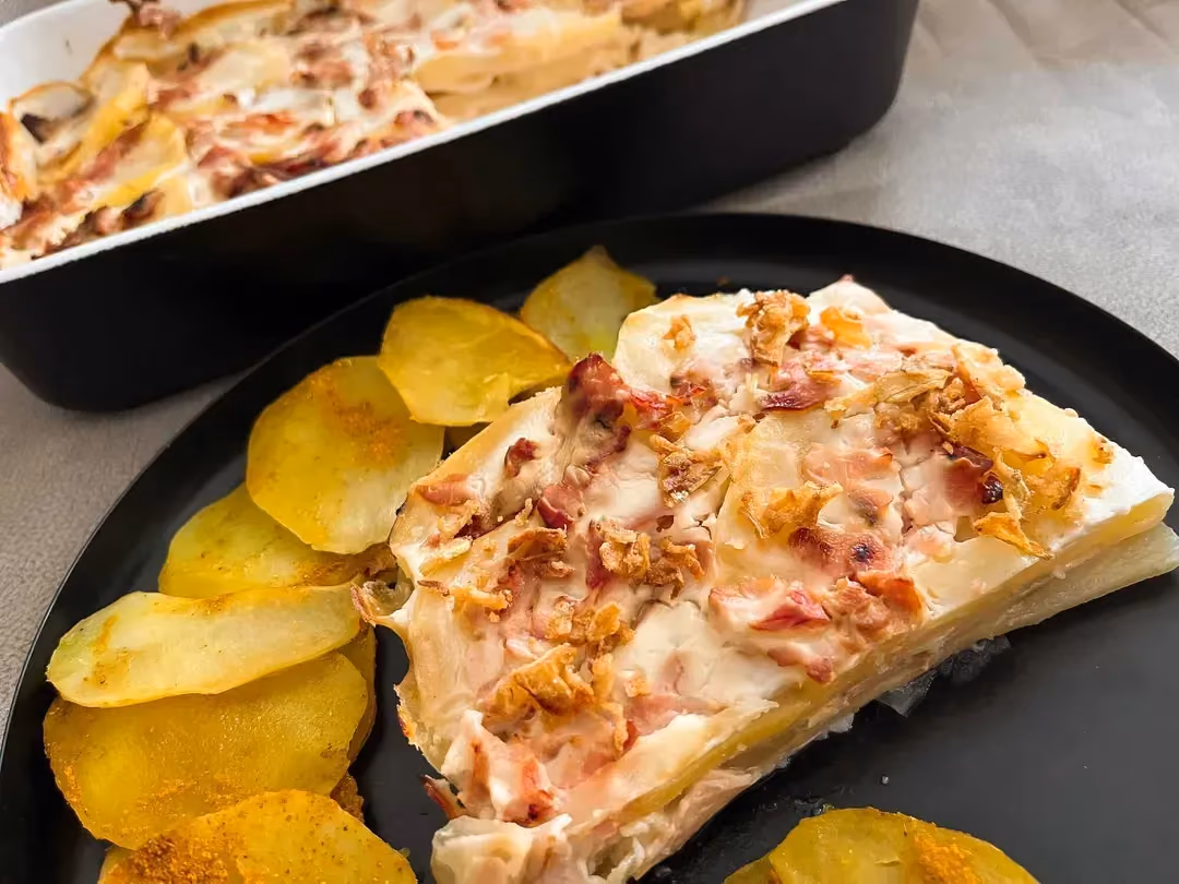 A baking dish contains lasagna-style potatoes, and in another dish in front there are thin slices of potato prepared like chips.