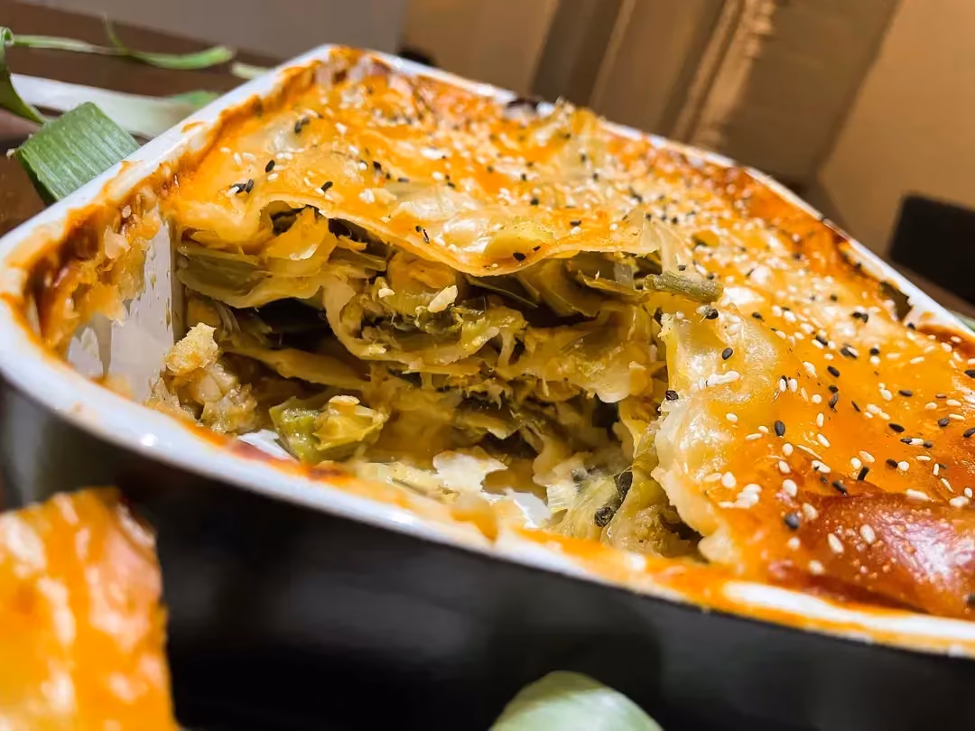 Dans un plat à gratin se trouve les lasagnes recouverts d'une couche de crème Béchamel. Une grosse partie a déjà été prélevée.