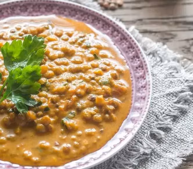 In a beautiful earthenware dish, the lentils are sitting in the sauce. A small sprig of parsley is visible on top.