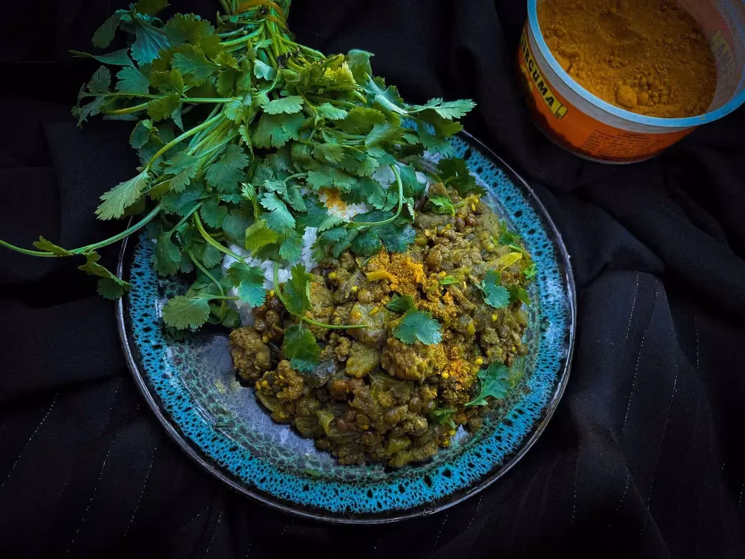 Une assiette plate de couleur bleu joliment décorée sert d'écrin à cet recette de lentilles aux aubergines et viande hachée.
