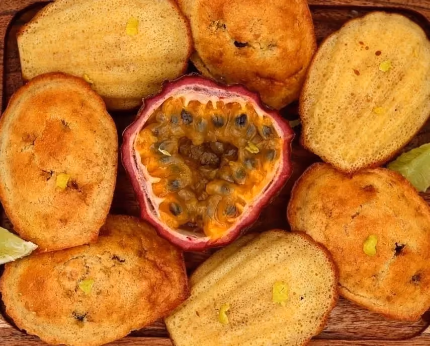 Six belles madeleines bien dorées entoure un maracudja coupé en deux.