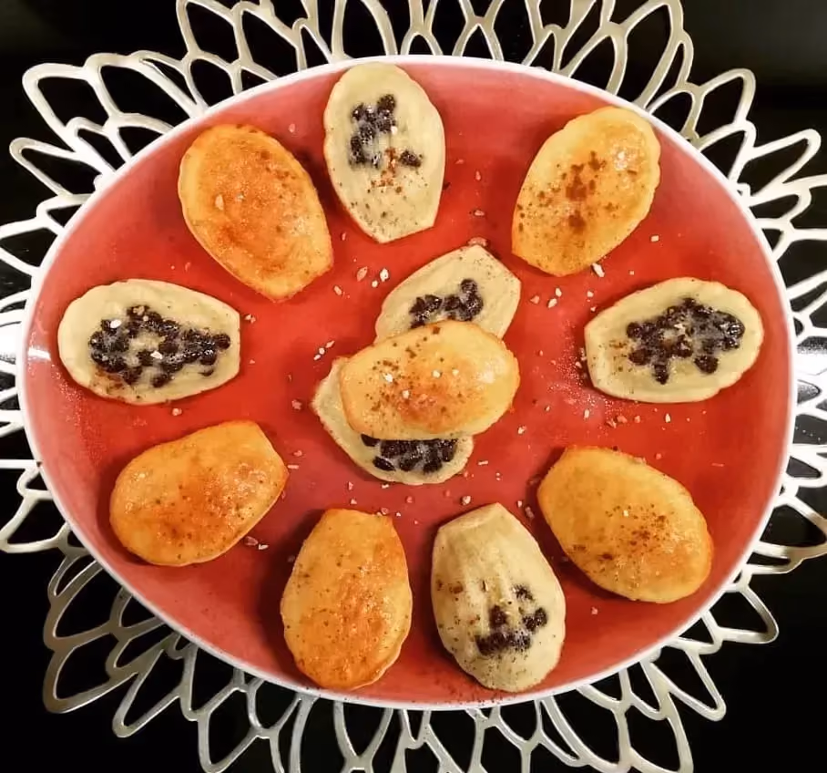 Disposés sur une assiette de couleur orange, six madeleines bien dorées sont coupées en deux. Les petites de chocolat sont bien présentes.