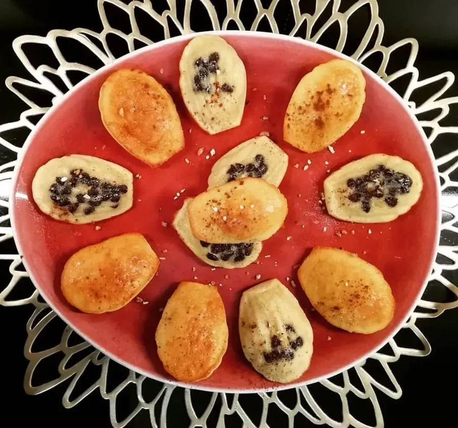 Arranged on an orange plate, six nicely golden madeleines are cut in half. The chocolate chips are clearly visible.