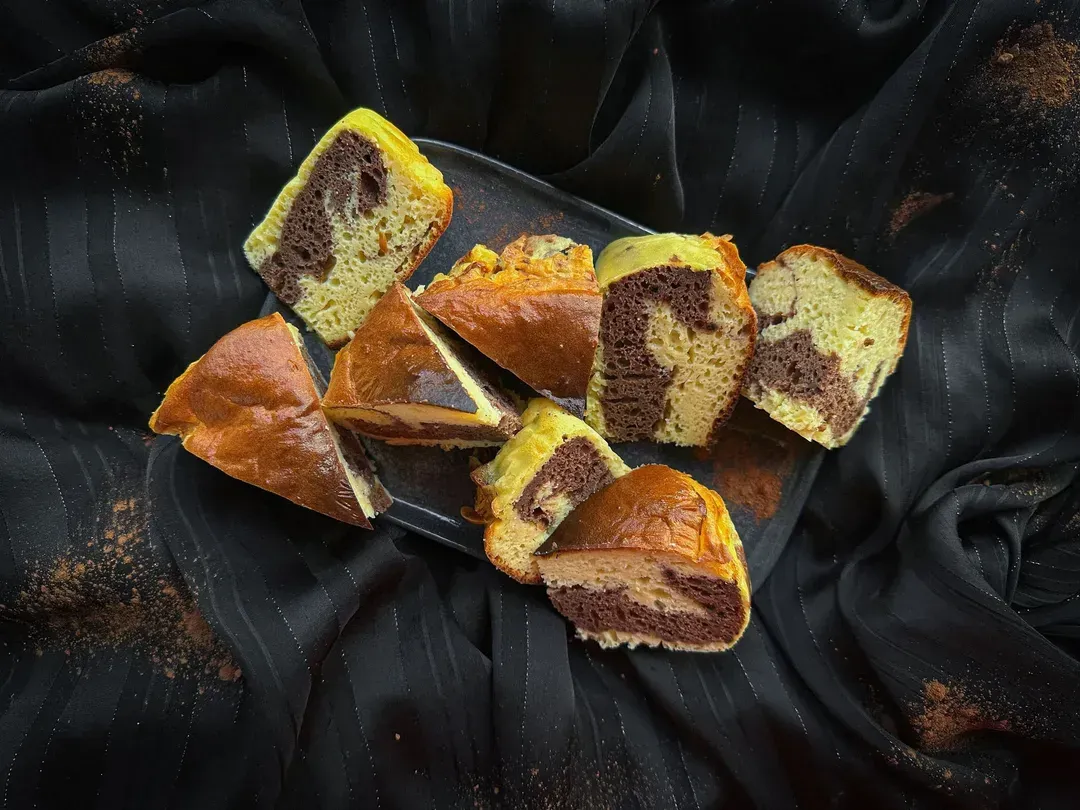 On three stacked white plates, there are three slices of protein chocolate marble cake. The topping is finished with two beautiful blackberries.