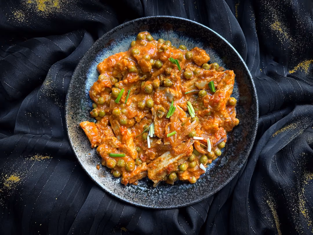 Le soja est cuisiné comme un curry avec des petits pois et de la tomate, le tout est présenté dans une assiette noire et bleue.