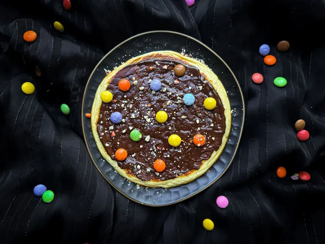 Smarties are arranged on top of the thick protein pancake. Slices of kiwi and mandarin segments are also present.