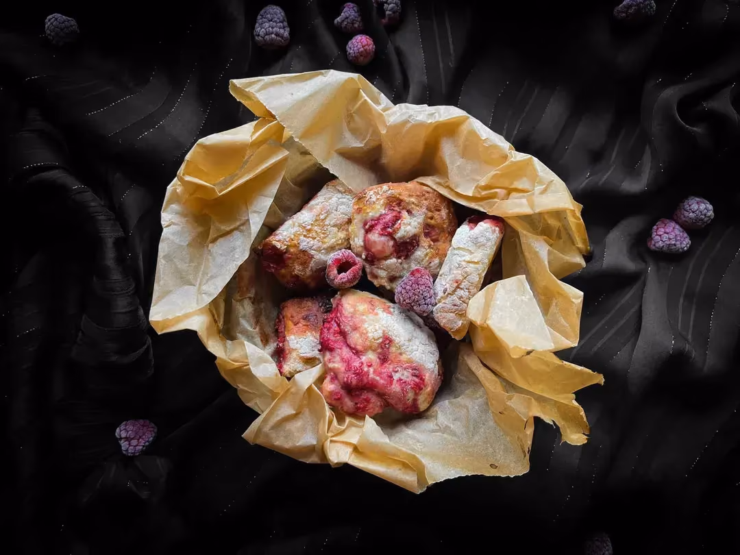 Les mini buns fourrés à la framboise sont déposés sur une serviette jaune qui tapisse un petit bol. Des framboises entières sont visibles au dessus.