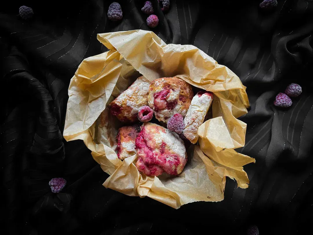 Mini raspberry-filled buns are placed on a yellow napkin lining a small bowl. Whole raspberries are visible on top.
