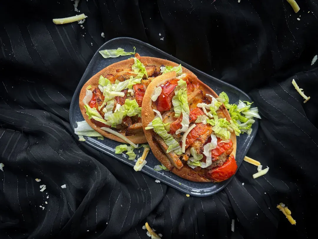 The three chicken pizzas, with tomato sauce and cheese, are presented on a wooden board and garnished with green onions.