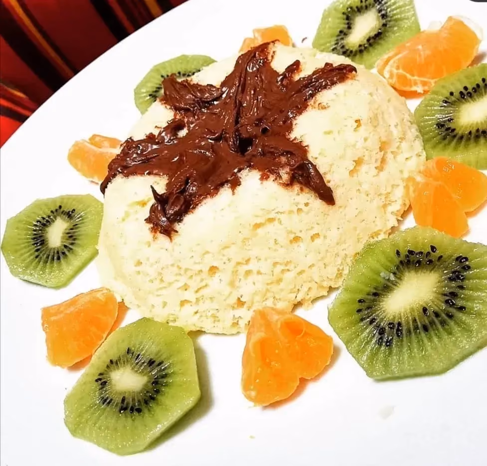 The vanilla cake is placed in the center of an oval plate. All around it, small kiwi slices and pieces of mandarin are arranged.