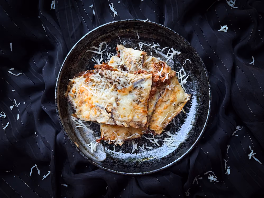 On a beige stoneware dish is moussaka, with its alternating layers of meat and eggplant. Topped with browned, melted cheese.