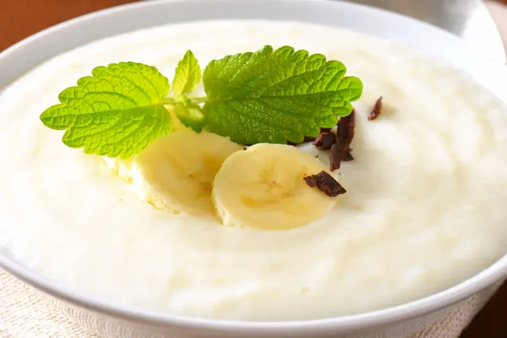 In a shallow white dish is the banana mousse. A few mint leaves accompany the dessert.