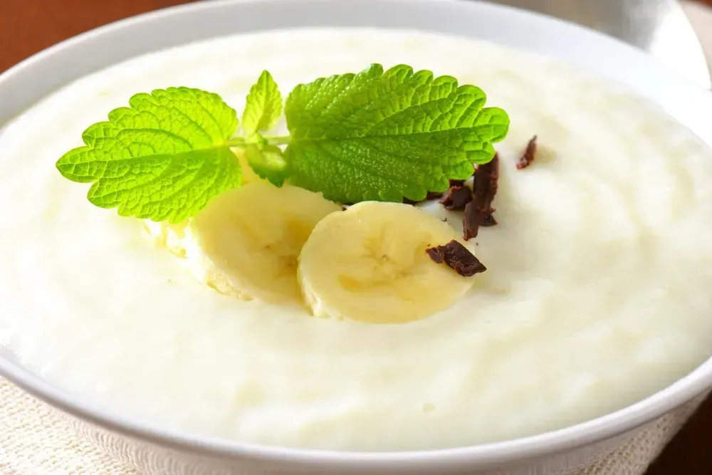 In a shallow white dish is the banana mousse. A few mint leaves accompany the dessert.