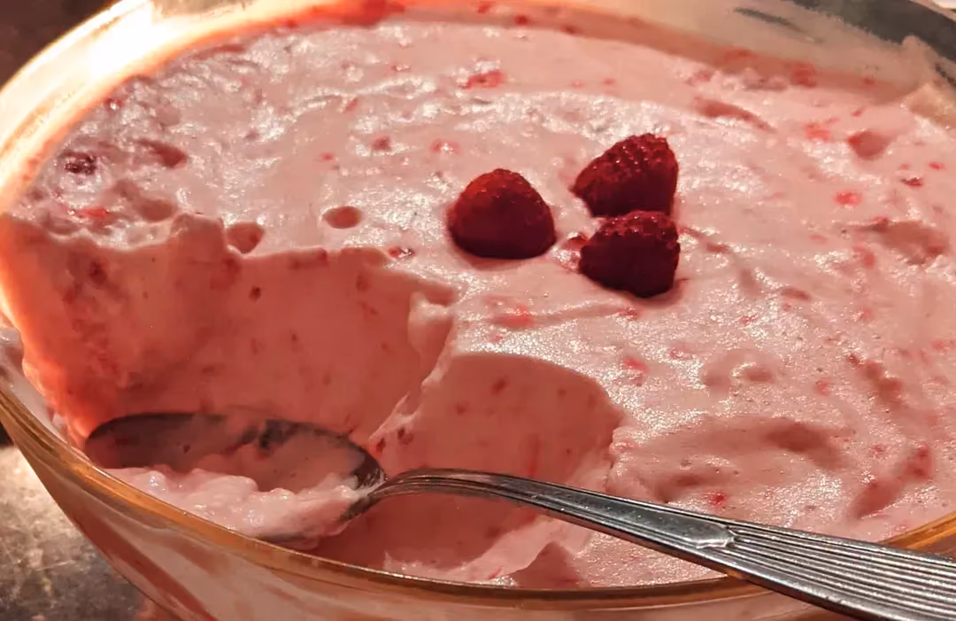 Dans un saladier, on retrouve la mousse à la framboise. Une grosse part a été prélevée. Trois framboises sont disposées sur le dessus de la mousse.
