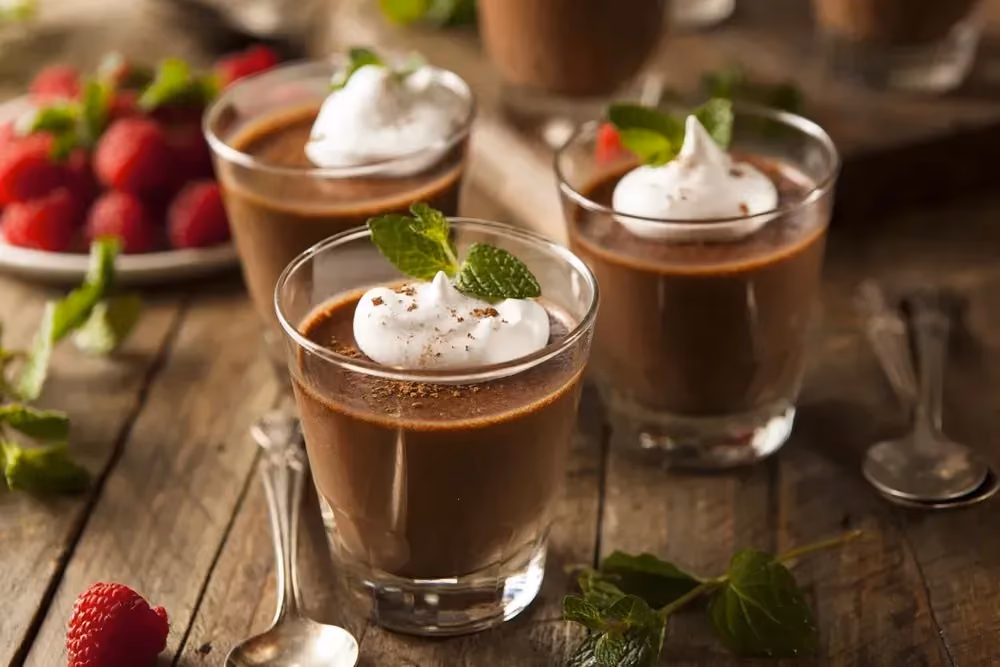 Sur une table en bois, sont disposés trois verrines contenant la mousse au chocolat. Le topping est composé de crème fraîche et feuilles de menthe.