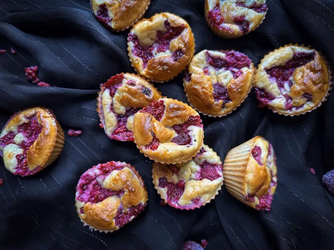 Sur une planche à découper en bois sont disposés cinq beaux muffins à la banane et à la framboise.
