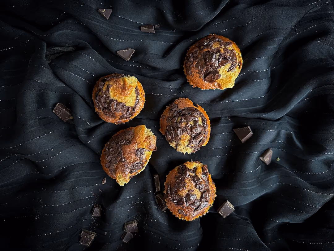 Des muffins posés sur un fond noir bien dorés et recouverts par du chocolat noir concassé en petits morceaux.