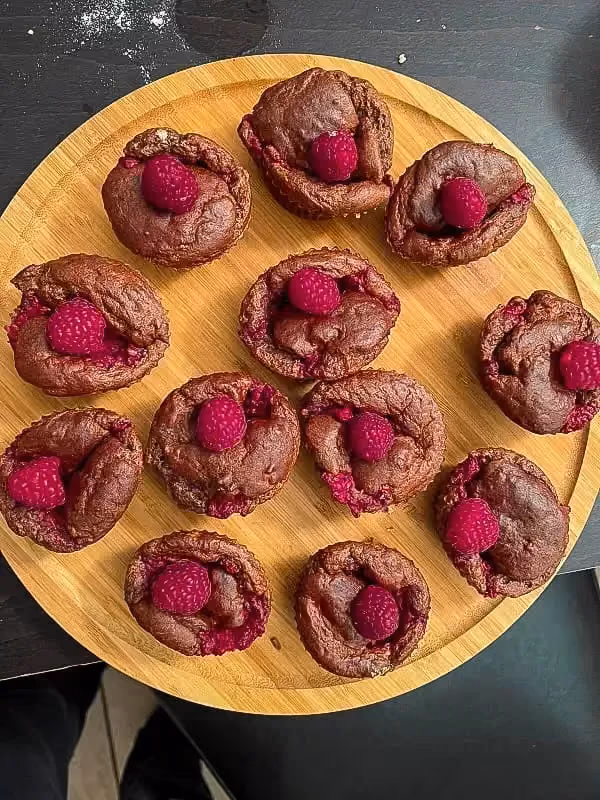 Dans un moule en papier, un muffin banane et chocolat montre sa plus belle robe. Une grosse framboise trône sur le dessus.