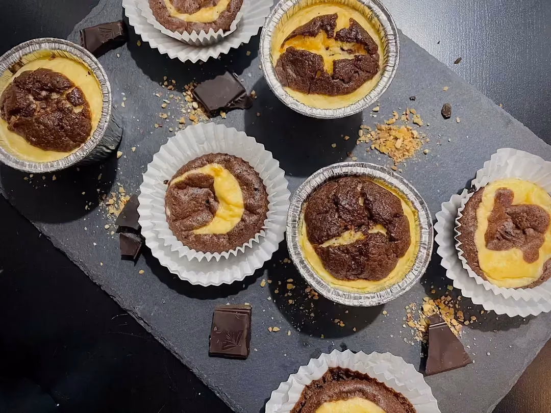 Sur une plaque de cuisson sont disposés les muffins. Certains sont démoulés et d'autres pas. Des carrés de chocolat accompagnent ce dessert moelleux.