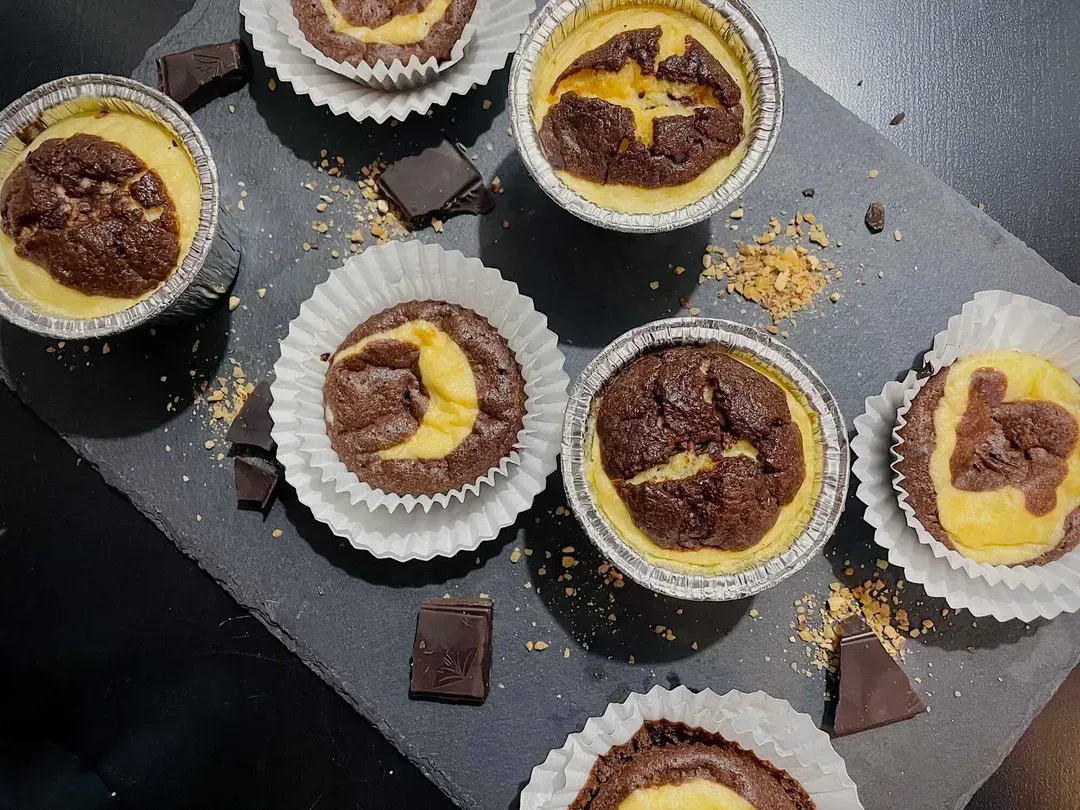 On a baking sheet, the muffins are arranged. Some are out of their molds and others are not. Squares of chocolate accompany this soft dessert.