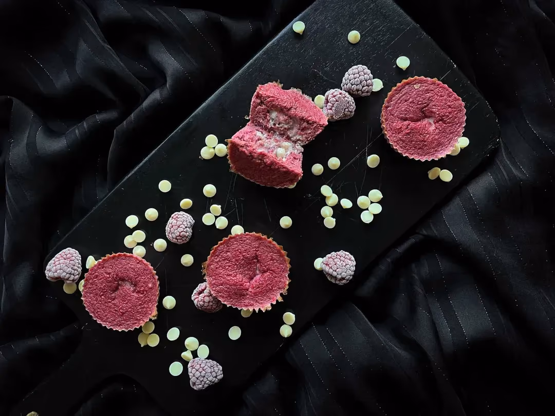 Cinq muffins fondants à la framboise et au chocolat sont disposés sur une planche à découper de couleur noire.