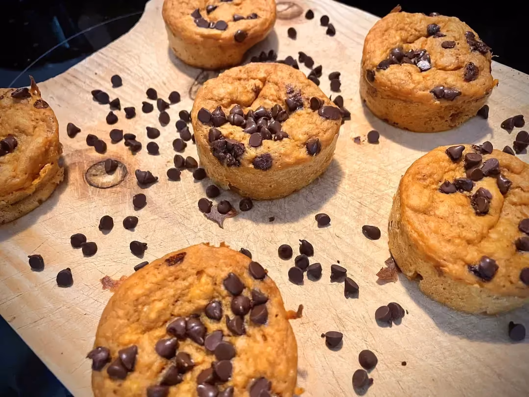 Sur un plateau de bois clair sont disposés six beaux muffins bien dorés saupoudrés de pépites de chocolat.