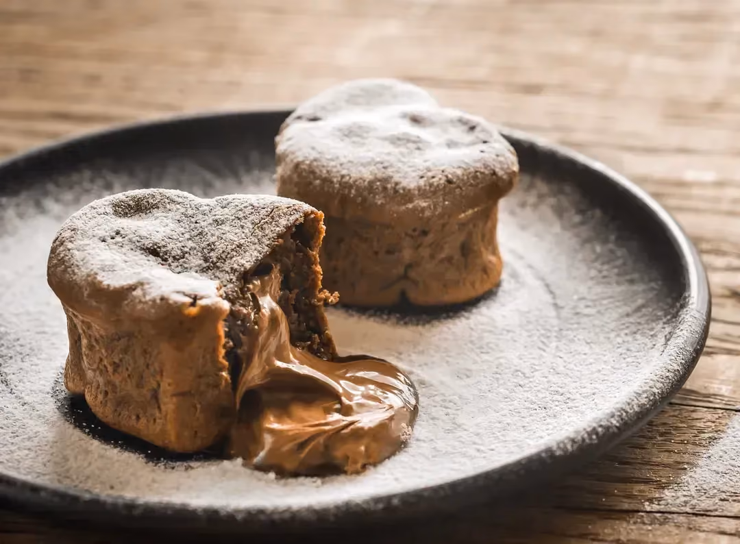 Dans un plat creux se trouve deux muffins dont l'un montre son coeur coulant, ils sont recouverts par du sucre glace.