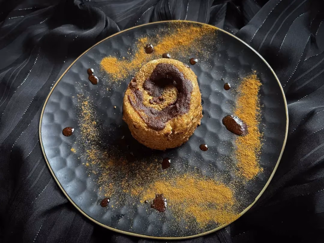 The cinnamon roll mugcake is presented on a beautiful blue honeycomb-patterned plate. It looks like a marble cake with its light and dark tones.