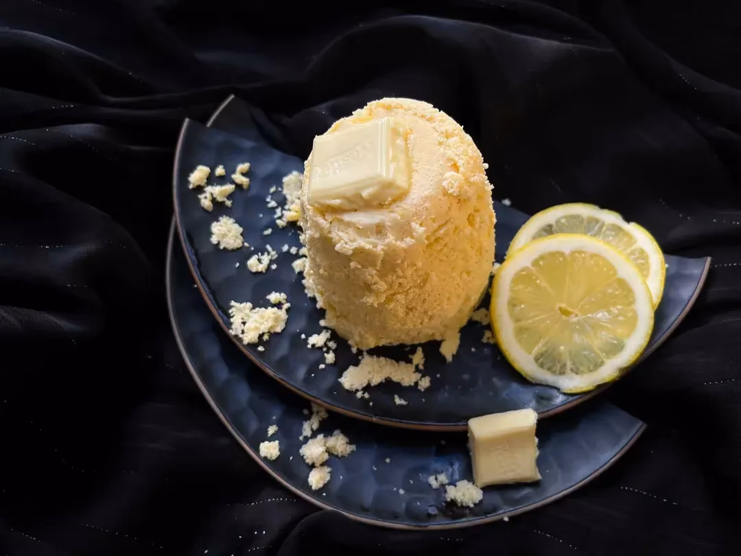 On a beautiful blue plate is the lemon and white chocolate mug cake. Next to it, you can see two slices of yellow lemon.