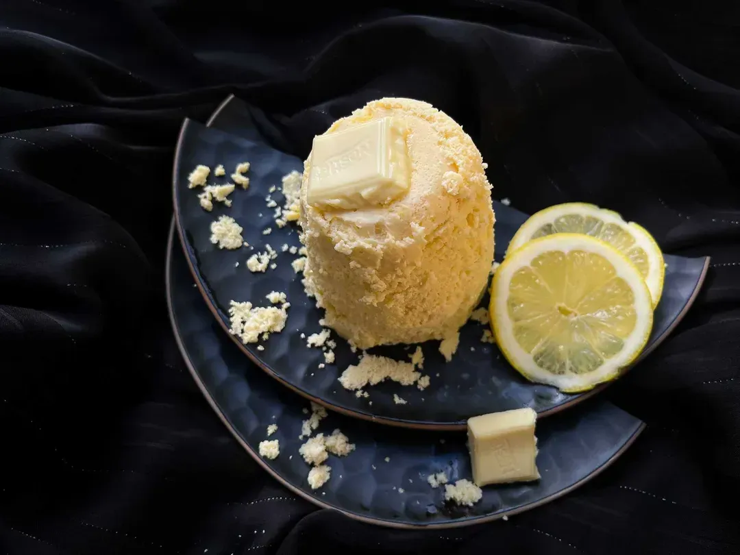 On a beautiful blue plate is the lemon and white chocolate mug cake. Next to it, you can see two slices of yellow lemon.