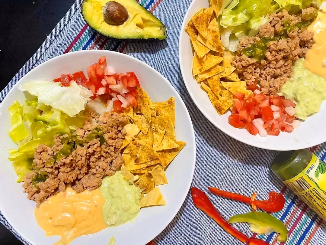 Sur une table sont disposées deux assiettes avec les nachos, les tomates, les oignons, la purée d'avocat et la viande de boeuf hachée.