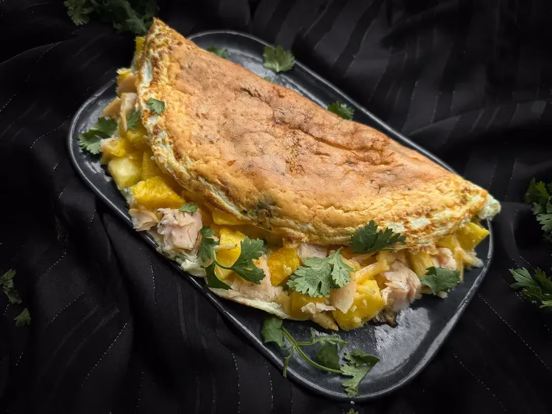Sur une assiette de couleur blanche, on peut voit l'omelette hawaïenne pliée en deux qui laisse apparaître l'ananas et le poulet coupés en petits dés