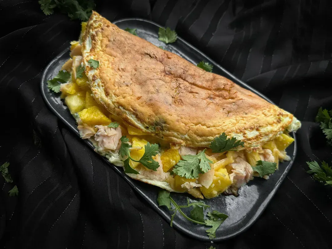 On a white plate, you can see the Hawaiian omelet folded in half, revealing the pineapple and chicken cut into small cubes