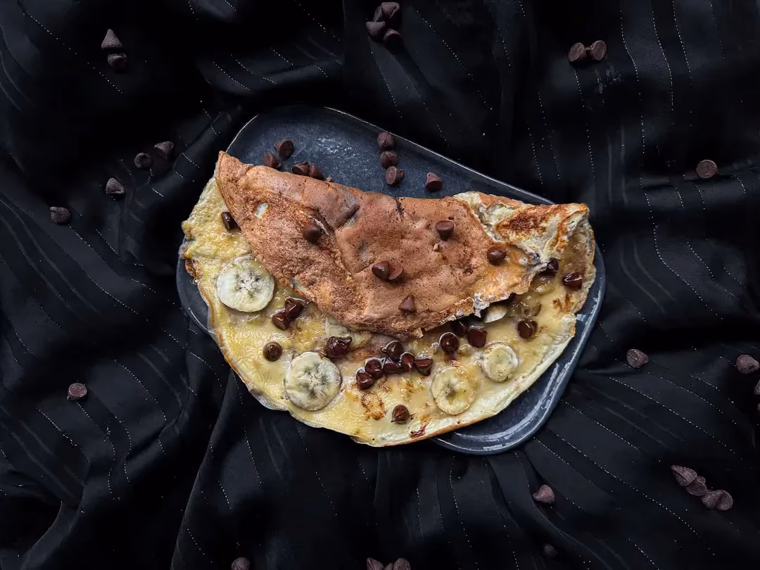 L'omelette sucrée à la banane et chocolat est pliée en deux sur sur une assiette de couleur verte.