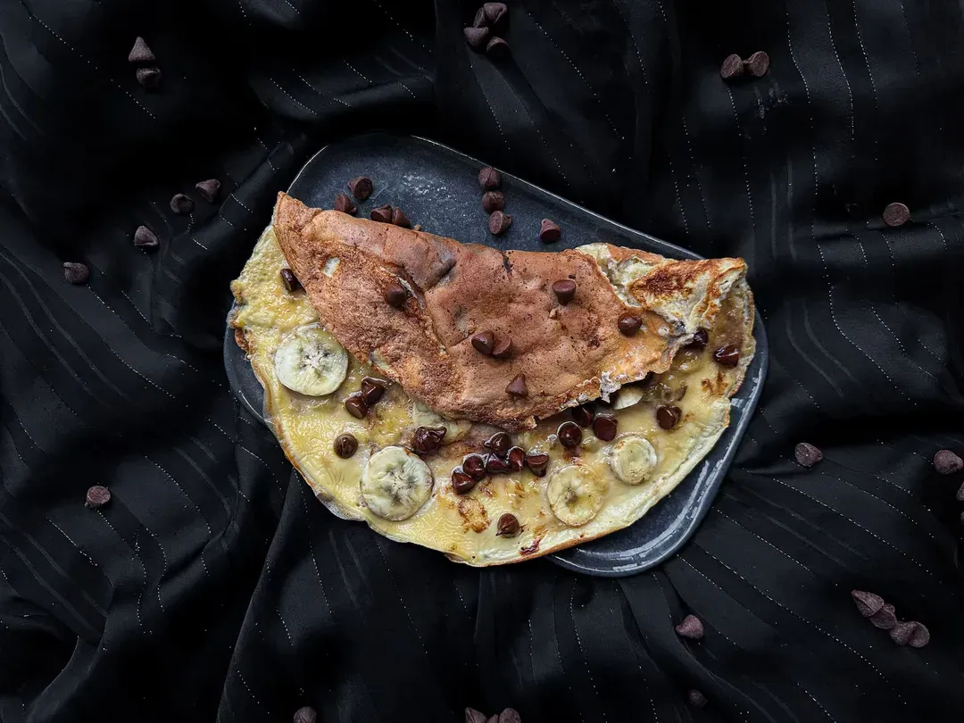 The sweet banana and chocolate omelet is folded in half on a green plate.