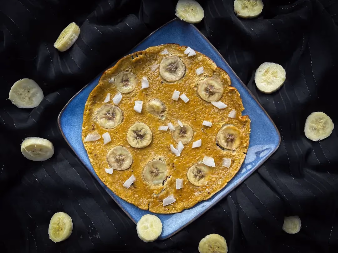 Sur une assiette carrée de couleur blanche se trouve l'omelette avec les petites rondelles de banane. De fins filets de chocolat servent de topping..