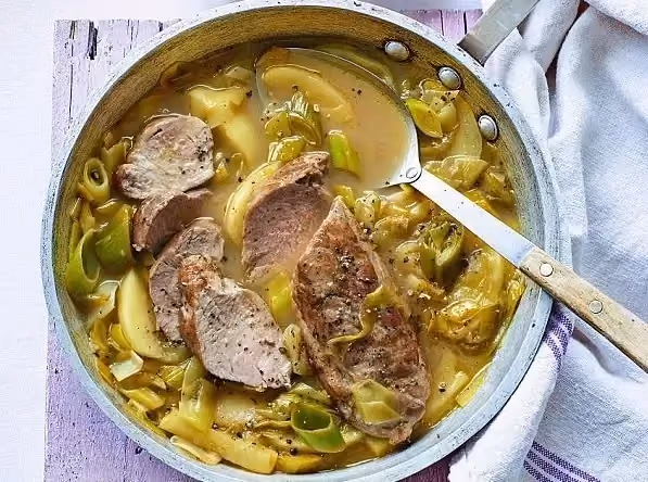 A spoon dips into the one-pot pork tenderloin, leeks, and apples.