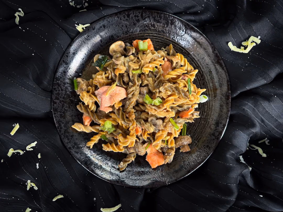 In a small blue earthenware bowl, there is a one-pot pasta made with smoked salmon, mozzarella, and button mushrooms.