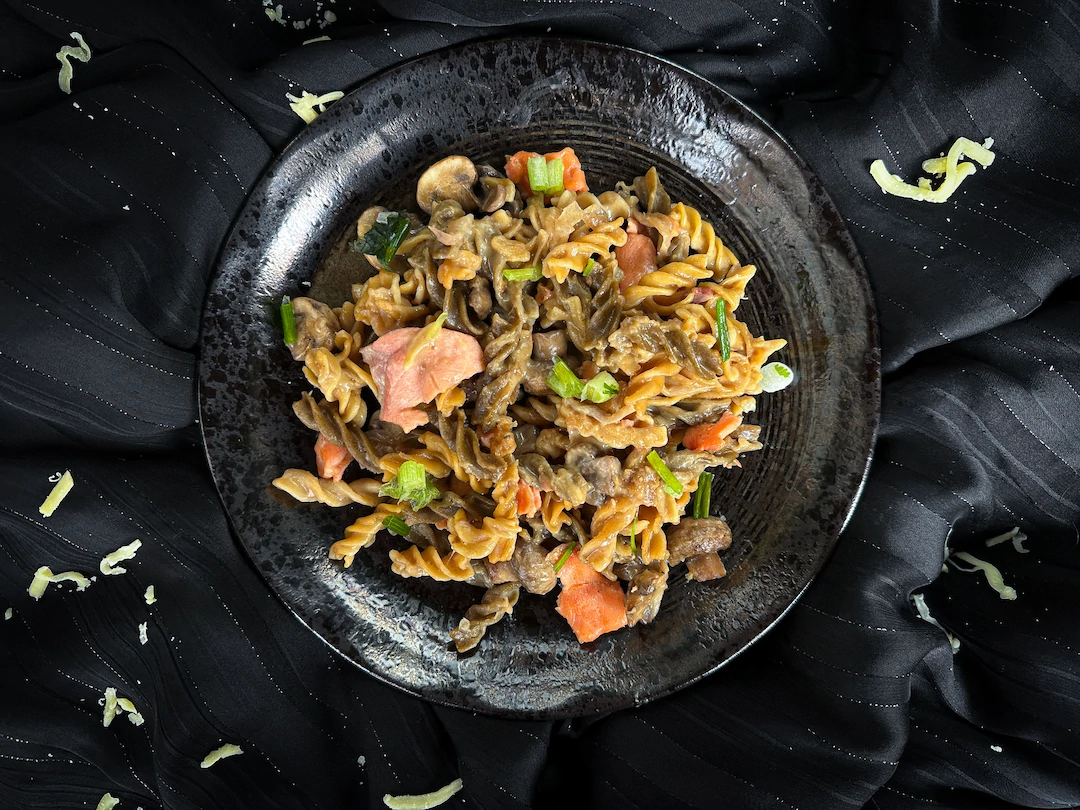 In a small blue earthenware bowl, there is a one-pot pasta made with smoked salmon, mozzarella, and button mushrooms.