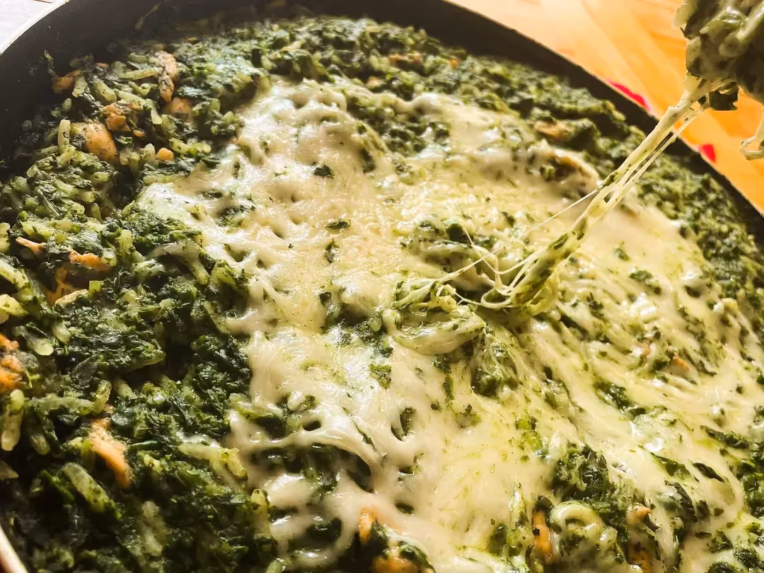 Spinach rice is arranged in a skillet with a melted cheese center.